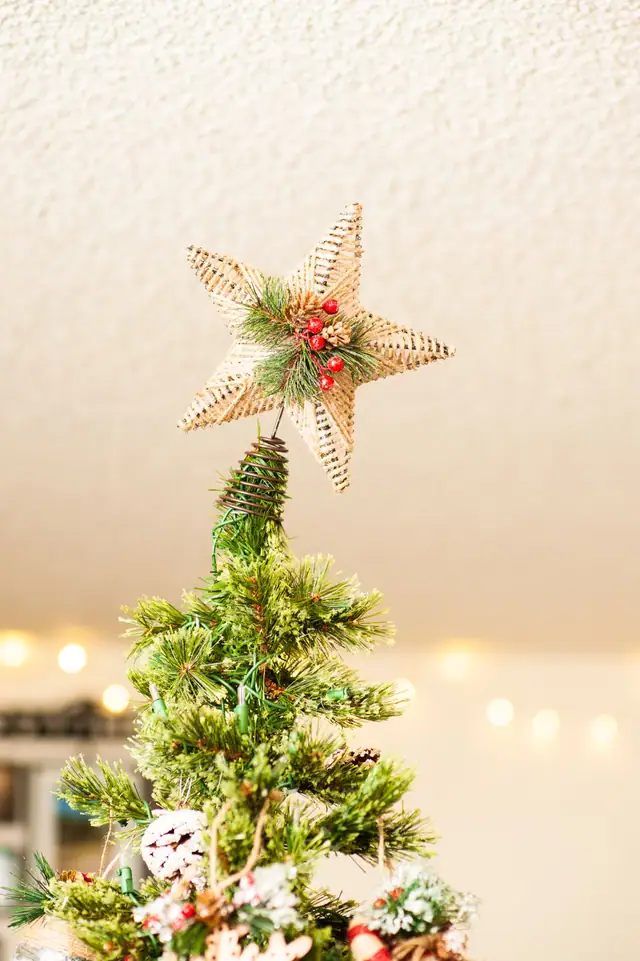 A rustic burlap star tree topper with red berries on a Christmas tree