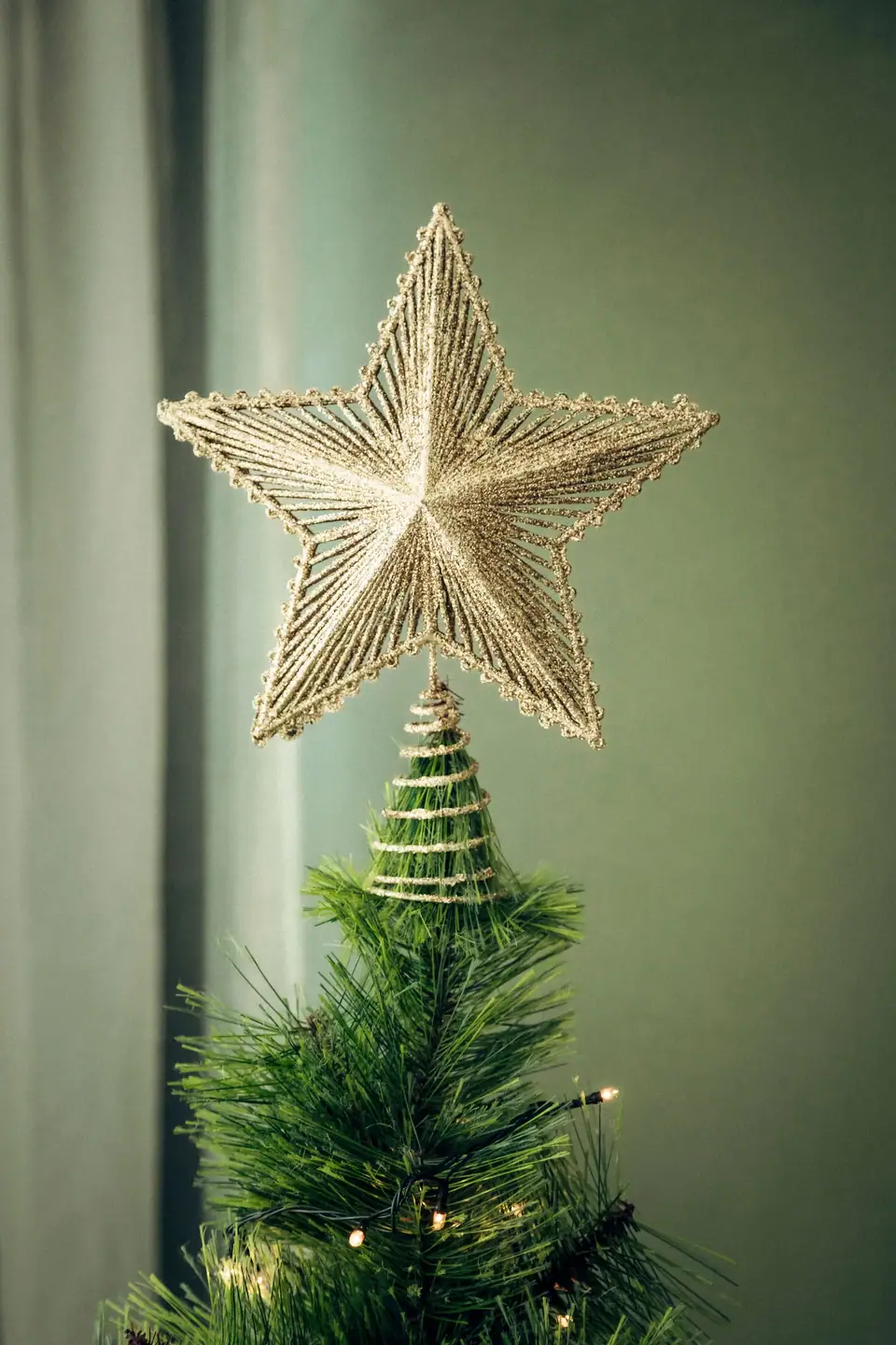 A gold glitter star topper on the top branches of an artificial Christmas tree